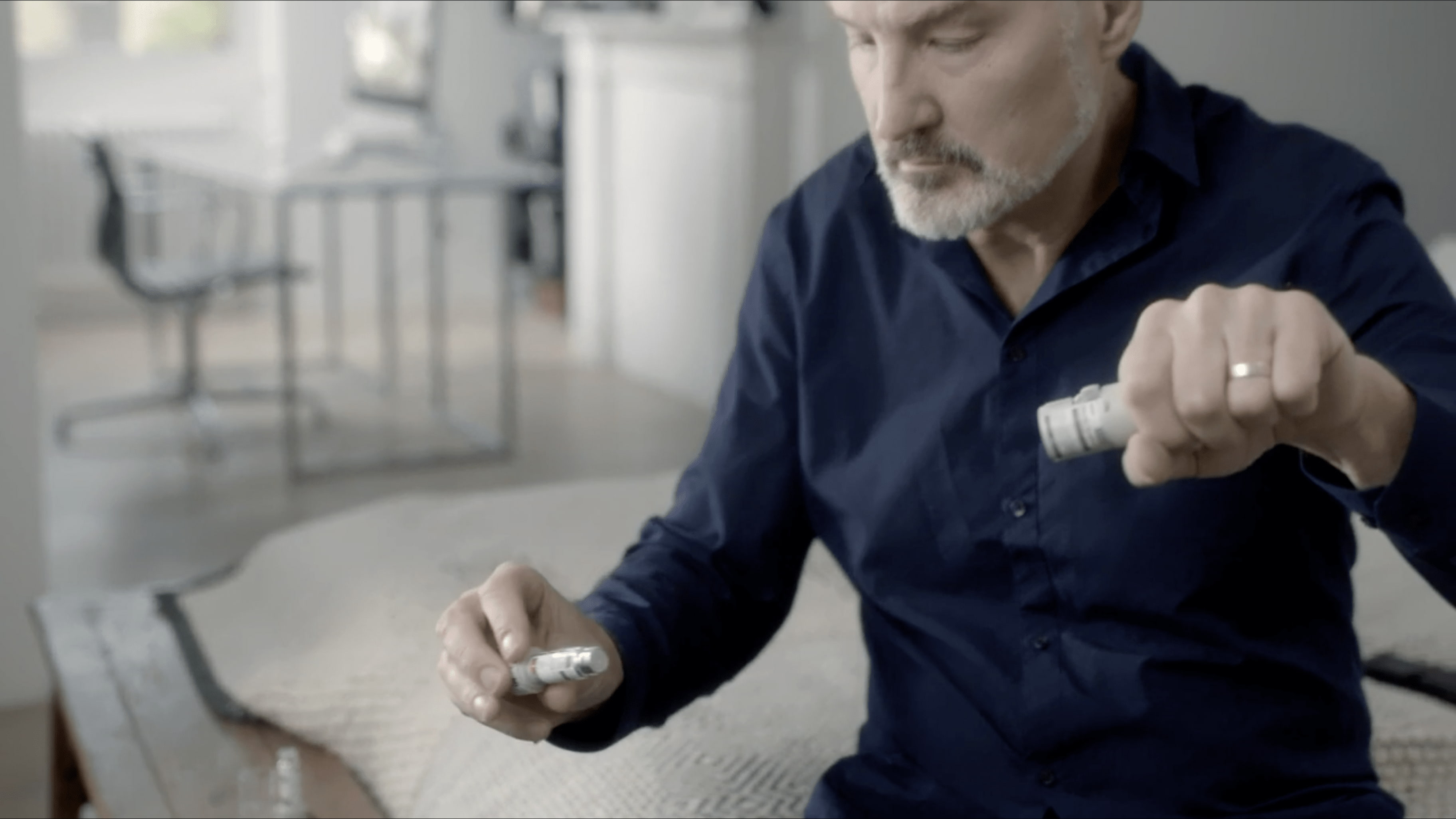 Muž sedí na posteli a uvoľnuje náplň z inhalátora za účelom vsunutia novej náplne